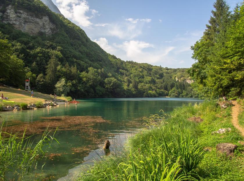 Lago alpino con vegetazione lussureggiante e persone che si rilassano.