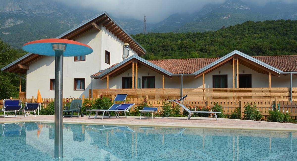 Piscina con sdraio davanti a un edificio in montagna, cielo nuvoloso.