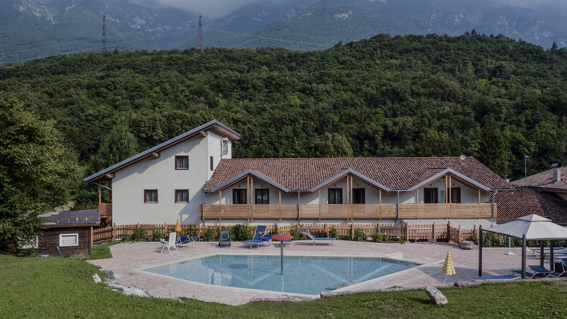 Casa di campagna con piscina e montagne sullo sfondo, circondata da verde.