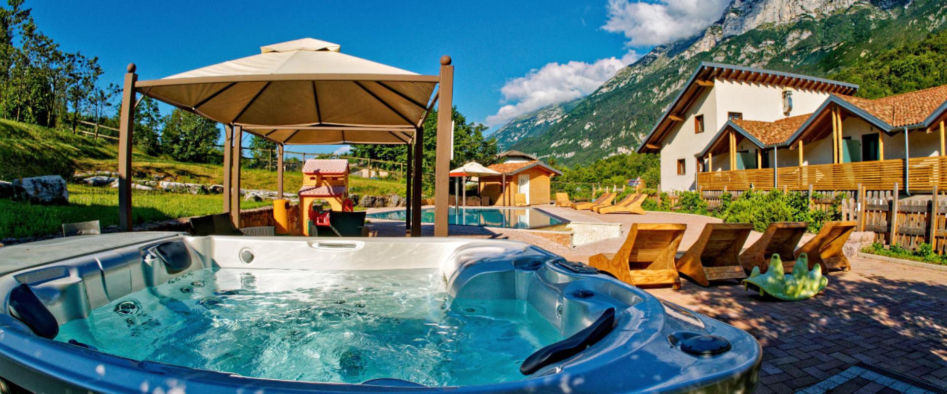 Vasca idromassaggio all'aperto con vista montagna, sedie a sdraio e gazebo.