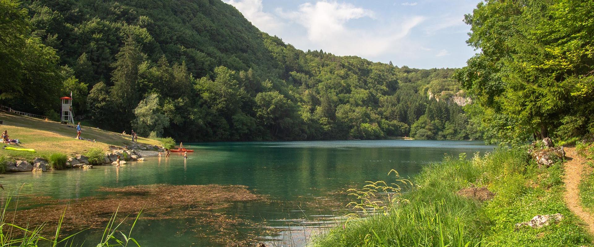 Lago circondato da colline verdi, con persone che si godono il paesaggio.