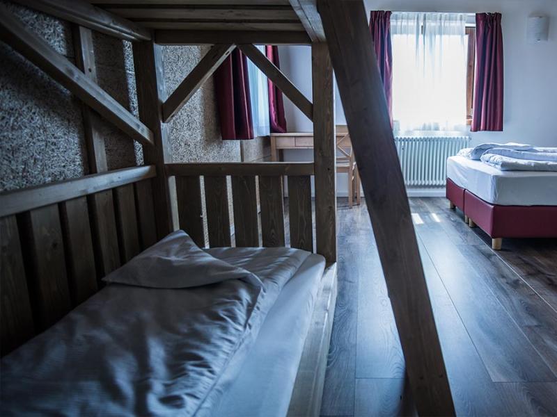 Camera con letto matrimoniale e letto a castello, pavimento in legno, tende rosse.