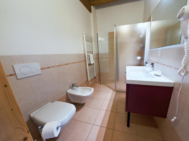 Bagno moderno con doccia, bidet, lavabo, asciugacapelli e sanitari su piastrelle beige.