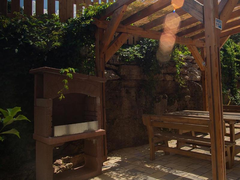 Area esterna con pergola in legno, tavolo e barbecue in muratura.