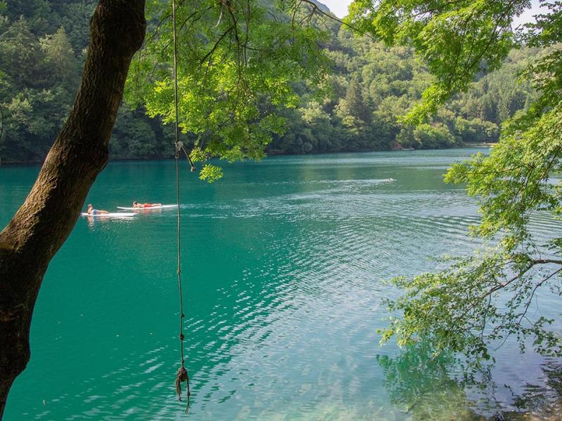 Lago turchese con persone su canoe, circondato da alberi verdi e natura rigogliosa.