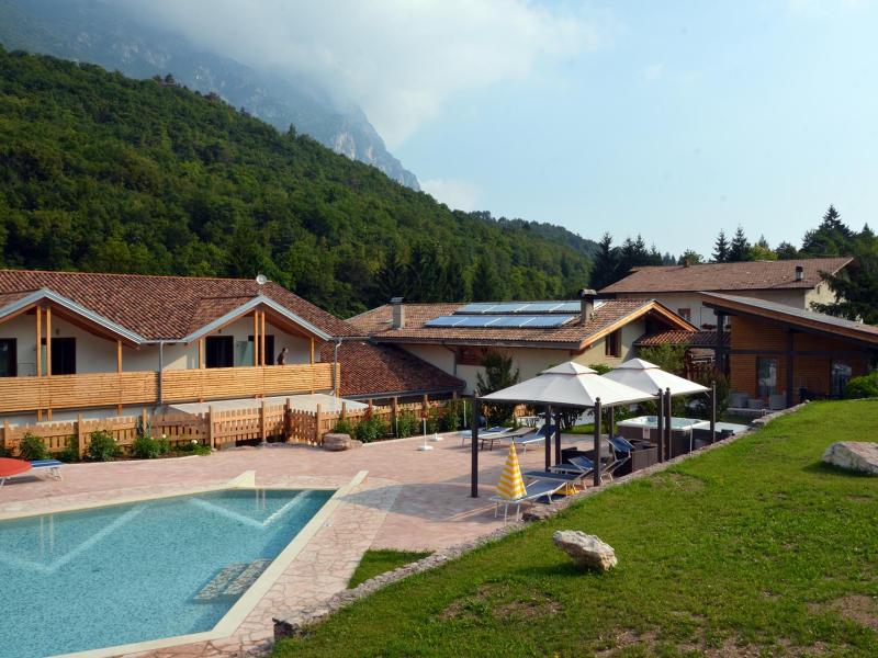 Baita con piscina, ombrelloni e pannelli solari immersa nel verde montano.