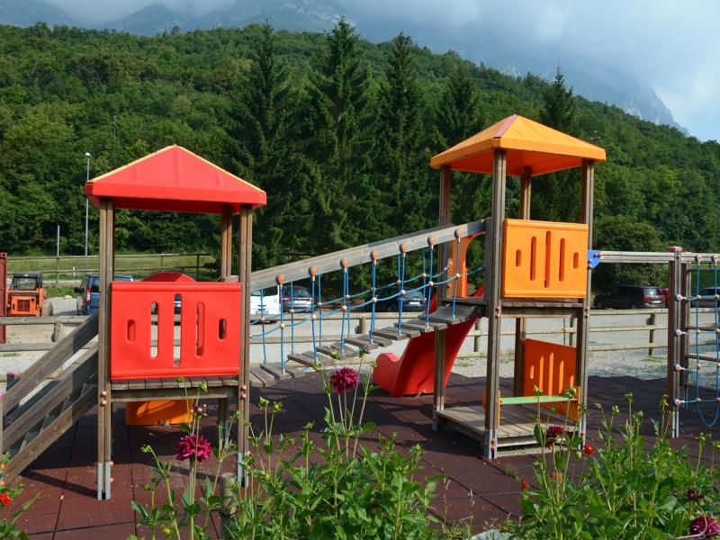 Parco giochi con scivolo e arrampicata, circondato da montagne e alberi.