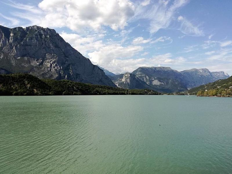 Lago verde smeraldo circondato da montagne imponenti sotto un cielo parzialmente nuvoloso.